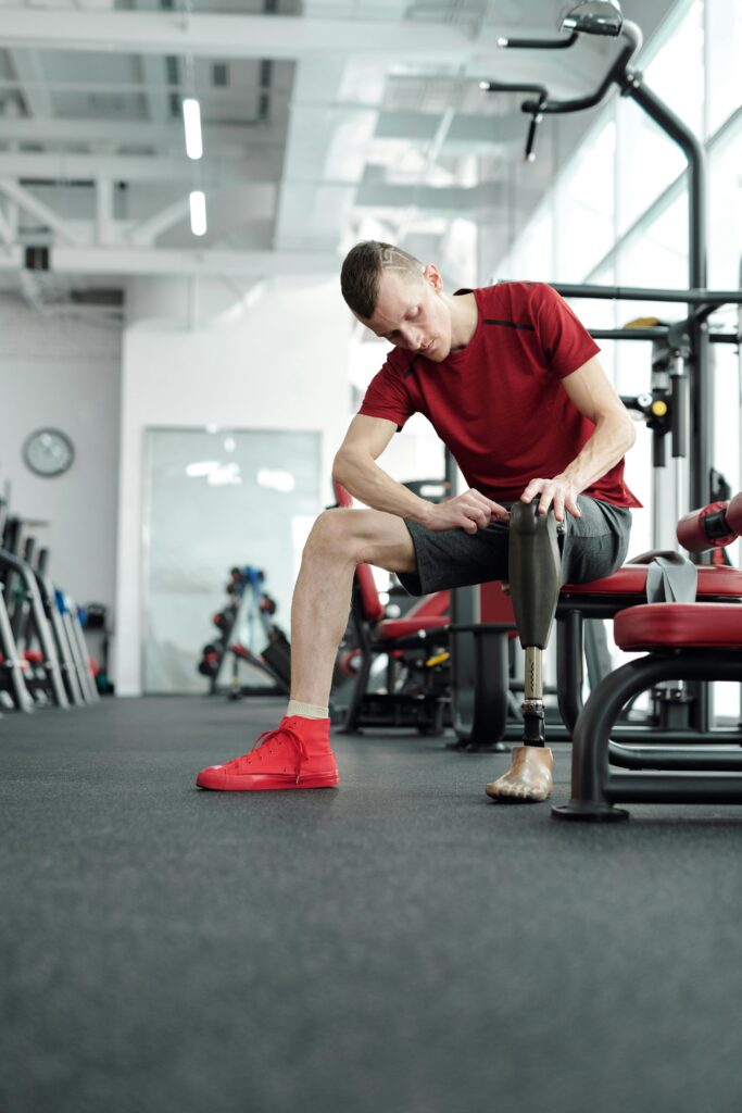 An empowered man adjusts his prosthetic leg while preparing for a workout in a modern gym.