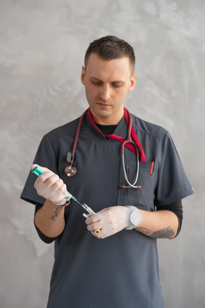 Healthcare professional in scrub suit preparing a syringe for medical procedure.